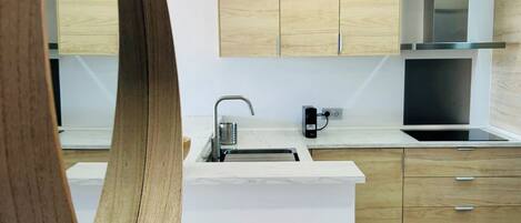 Une cuisine moderne avec des meubles en bois clair, un plan de travail blanc et une hotte de cuisine en acier inoxydable.