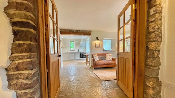 Pasillo con piso de piedra que conduce a una cocina y sala de estar con sofá de cuero.