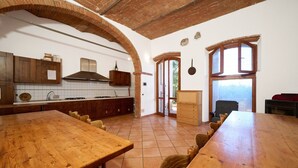A spacious kitchen with wooden cabinets, a large wooden table, and a view through a window.