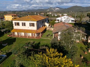 Une maison à deux étages dotée d’un patio couvert, entourée de verdure et avec une chaîne de montagnes en toile de fond.