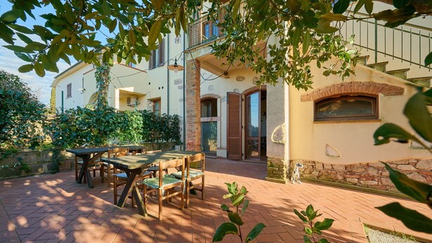 Eine Terrasse mit Tisch und Stühlen, eine Steinmauer und ein Gebäude mit Balkon.