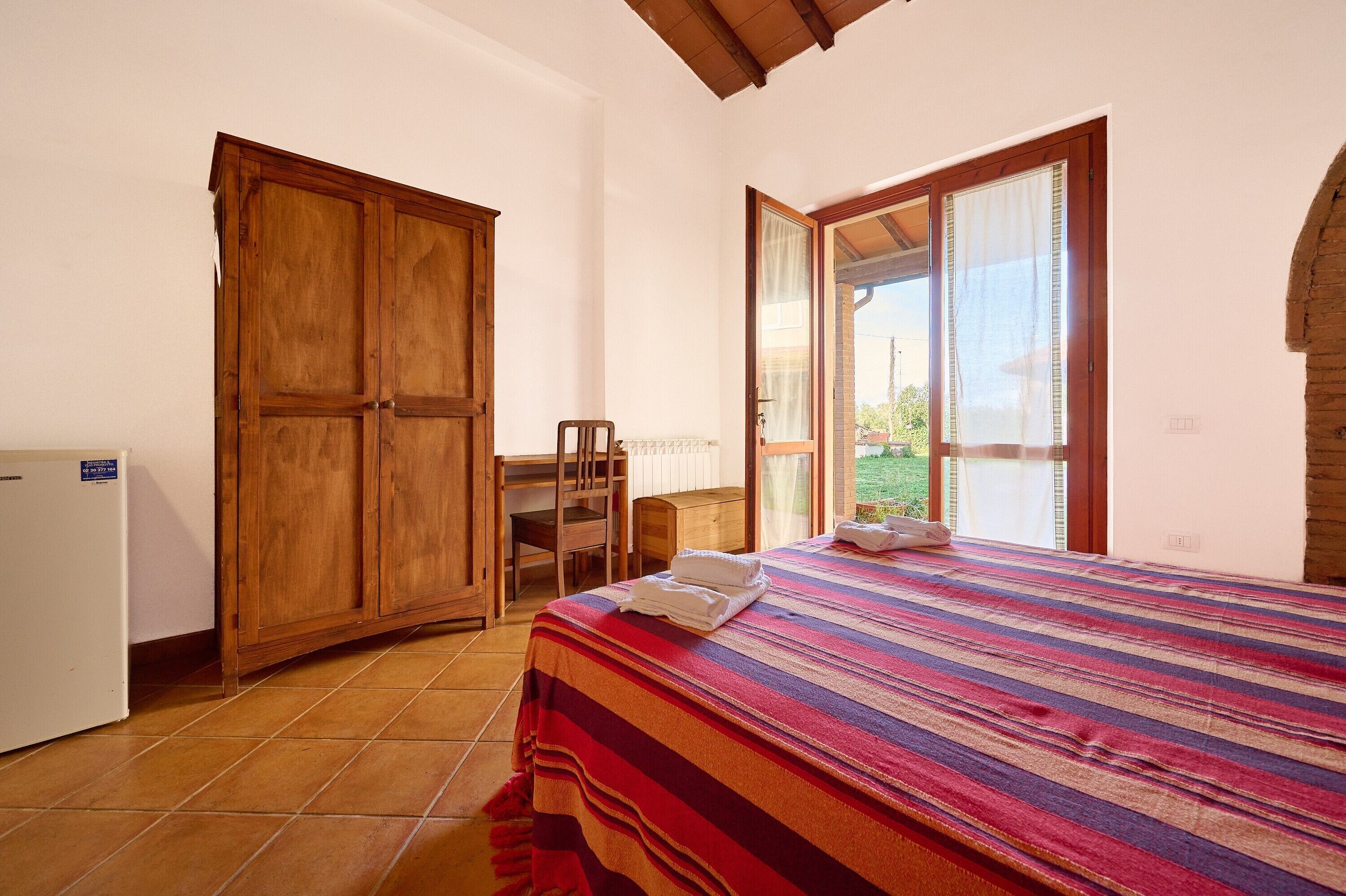A bedroom with a bed, a wooden wardrobe, a desk, and a chair.