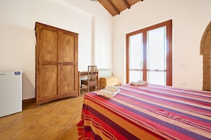 A bedroom with a bed, a wooden wardrobe, a desk with a chair, and a window with blinds.