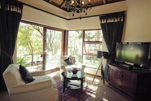 Sala de estar con sofá, una mesa de vidrio, televisor y vistas al exterior.