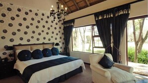 Een slaapkamer met een groot bed, een stoel, een kroonluchter en uitzicht op groen.