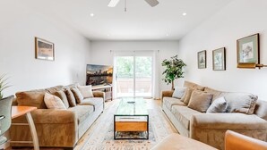 Un salon moderne avec deux canapés beige, une table basse en verre et une grande fenêtre donnant sur un paysage verdoyant.
