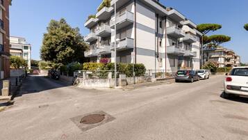 Un edificio residencial de varios pisos con balcones, entrada porticada y automóviles estacionados en un día despejado.