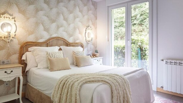 A bedroom with a large bed, white bedding, a fluffy beige throw, and a patterned wallpaper. - Txanka Erreka (Orio)