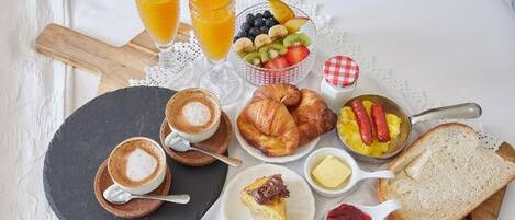 En frukostuppsättning med croissanter, frukt, sylt, smör, rostat bröd och kaffe på ett bord.