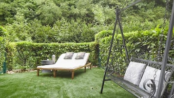 A garden with a wooden lounge chair and a metal swing chair.