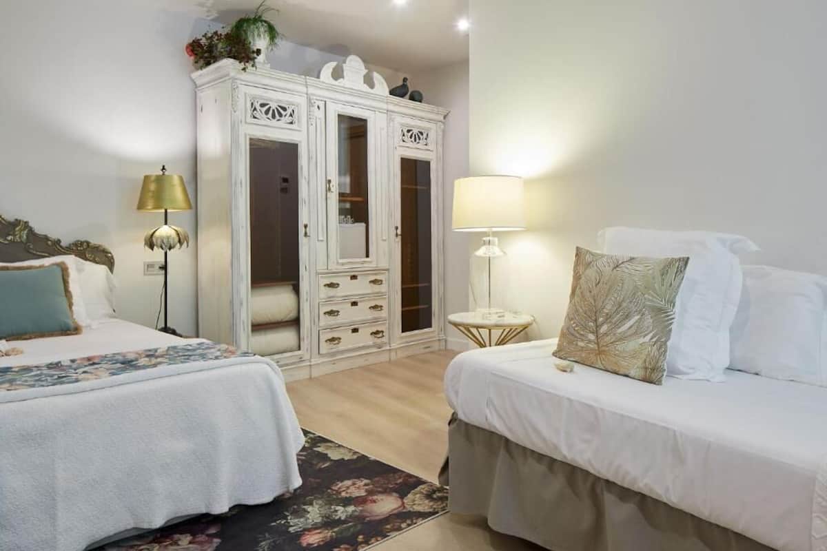 A bedroom with two beds, a wardrobe, and a small table with a lamp.