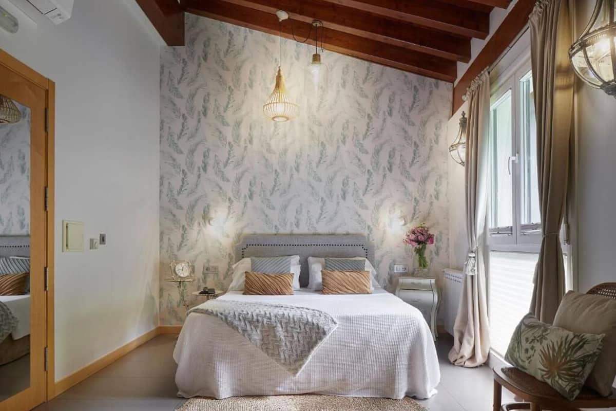 A bedroom with a large bed, a wooden ceiling, and a patterned wallpaper.