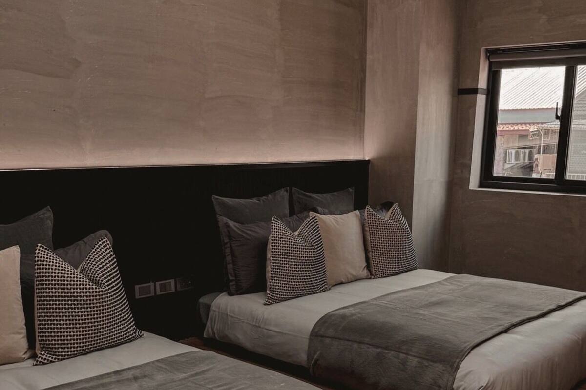 A modern bedroom with two beds, a large window, and a view of the city.