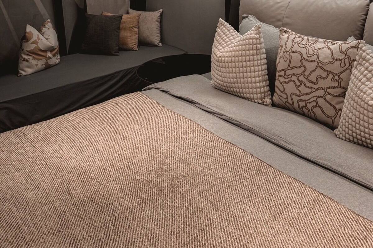 A modern bedroom with a bed, a seating area with cushions, a staircase, and a wall-mounted light fixture.