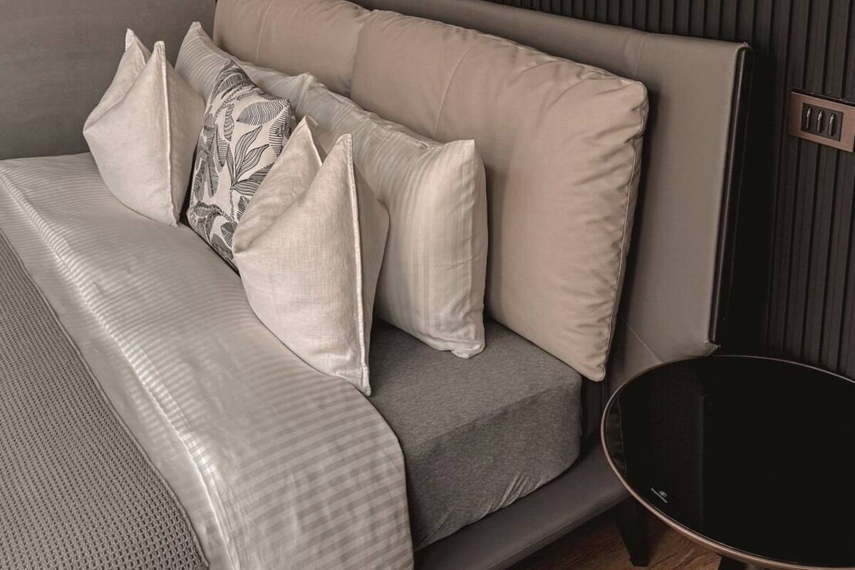 A modern bedroom with a bed, pillows, a blanket, a bedside table, and a wall-mounted air conditioner.