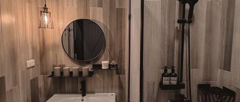 A modern bathroom with a wooden panel wall, a round mirror, a white sink, and a shower area.