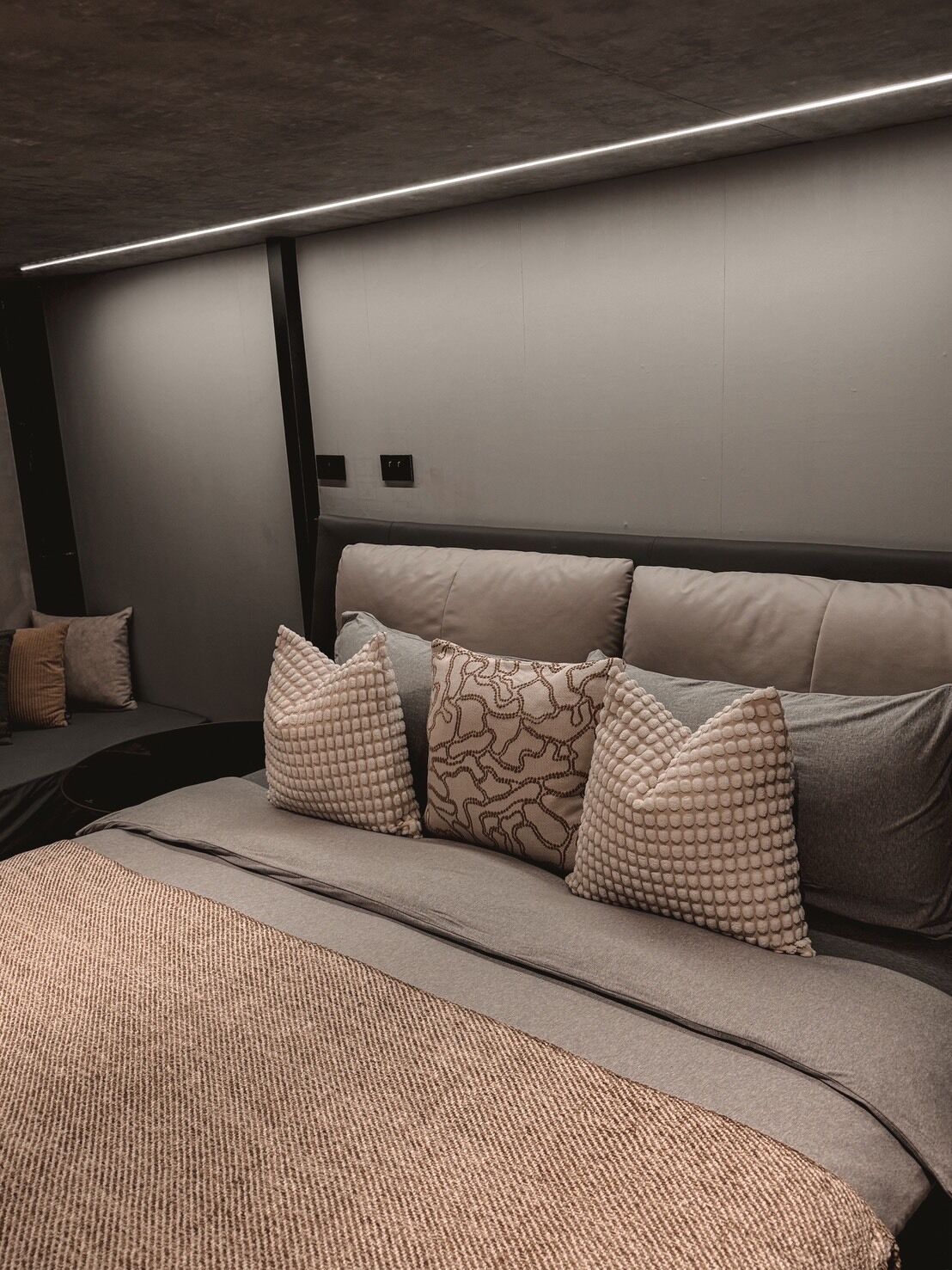 A modern bedroom with a large bed, multiple pillows, and a dark headboard.
