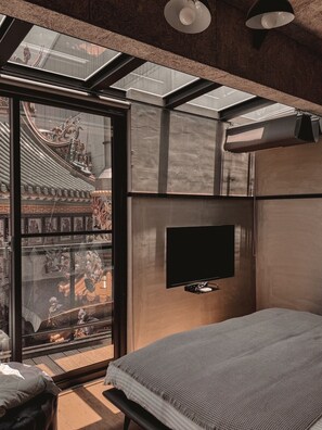 Ein modernes Schlafzimmer mit Dachfenster, einem Flachbildfernseher und einem Bett mit grauer Decke.