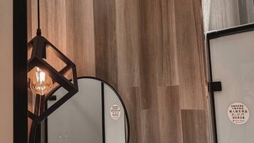 A bathroom with a round mirror, wooden panel walls, a hanging light fixture, and a shelf with toiletries.