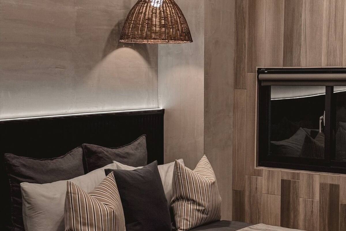 A modern bedroom with a large bed, a television mounted on the wall, and a woven pendant light.