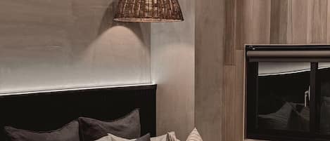 A modern bedroom with a large bed, a television mounted on the wall, and a woven pendant light.