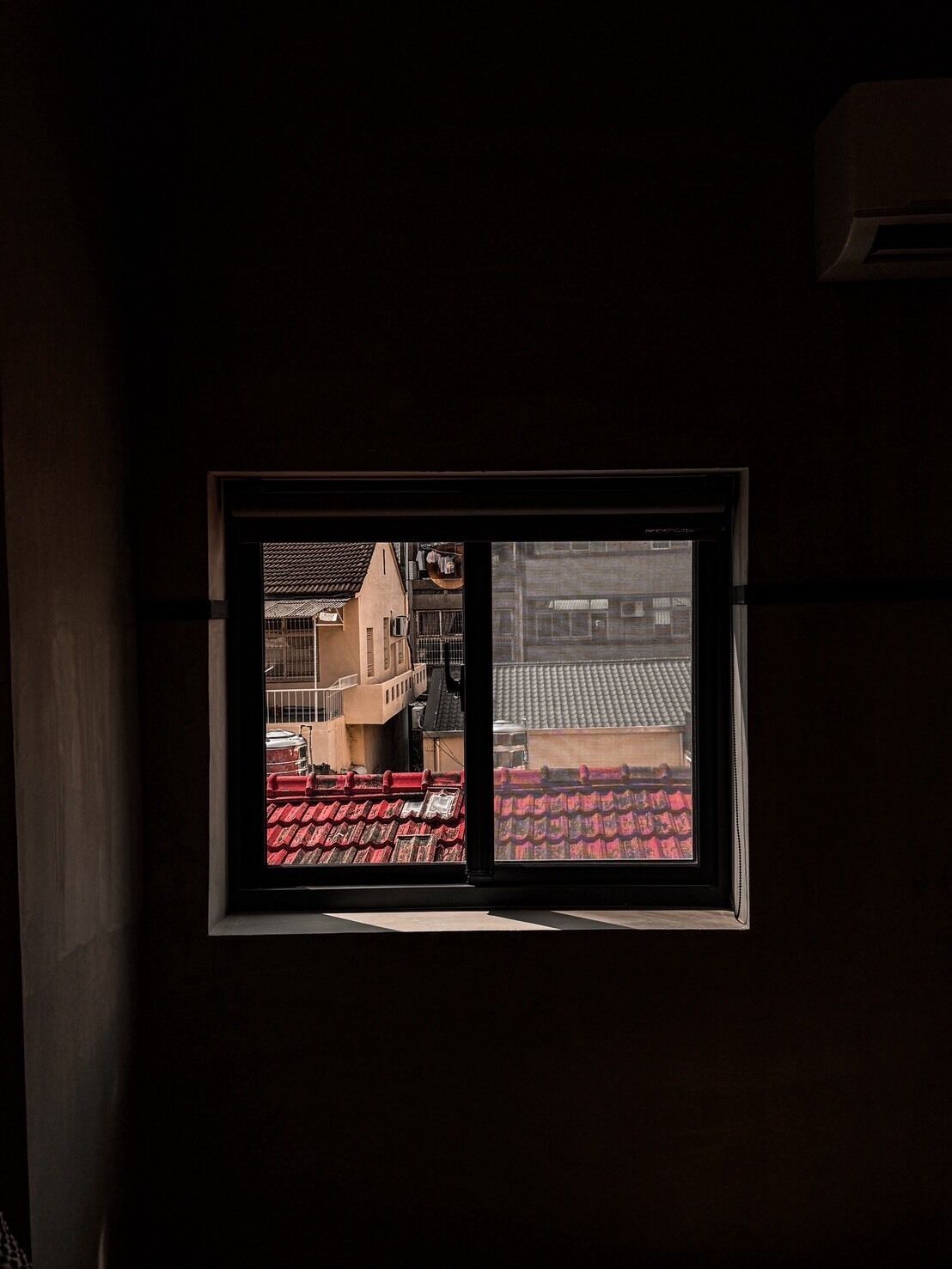 Uma janela com vista para um edifício com telhados vermelhos e uma varanda.