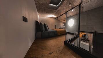 A modern bedroom with a loft bed, a glass-walled bathroom, and a wooden floor.