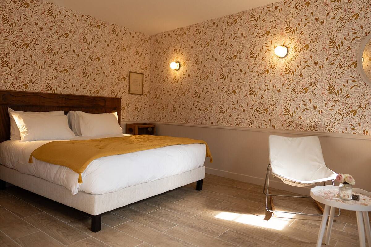 A bedroom with a large bed, a wooden headboard, two bedside tables, a chair, and a small table with a vase.