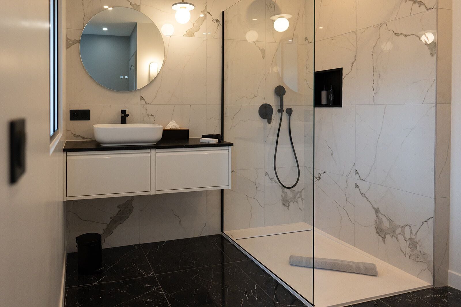 A modern bathroom with a white sink, a round mirror, and a glass-enclosed shower area.