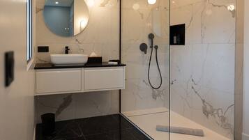 A modern bathroom with a white sink, a round mirror, and a glass-enclosed shower area.