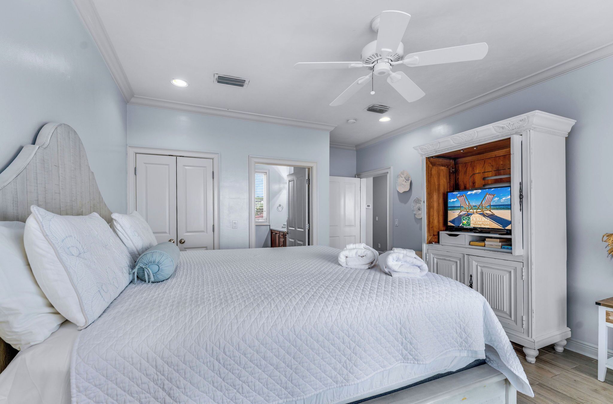 A bedroom with a large bed, white walls, a ceiling fan, and a television on a wooden cabinet.