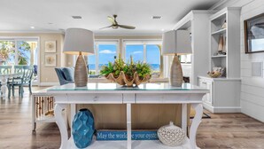 A modern kitchen with a glass-top dining table, white cabinetry, and a view of the ocean.