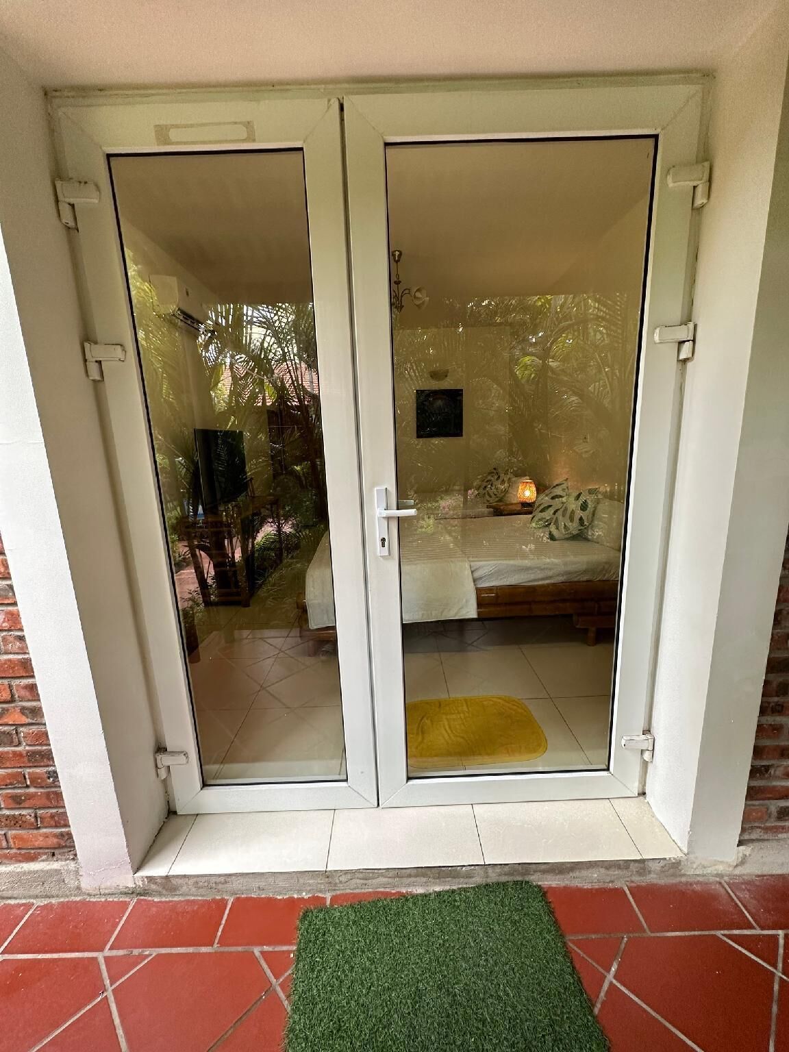 Une porte-fenêtre coulissante donne accès à une pièce qui contient un lit, un petit tapis et une table de chevet.