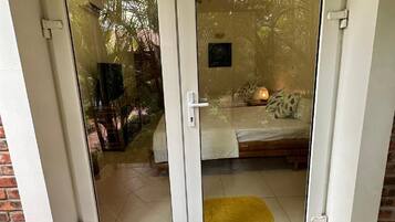 Une porte-fenêtre coulissante donne accès à une pièce qui contient un lit, un petit tapis et une table de chevet.