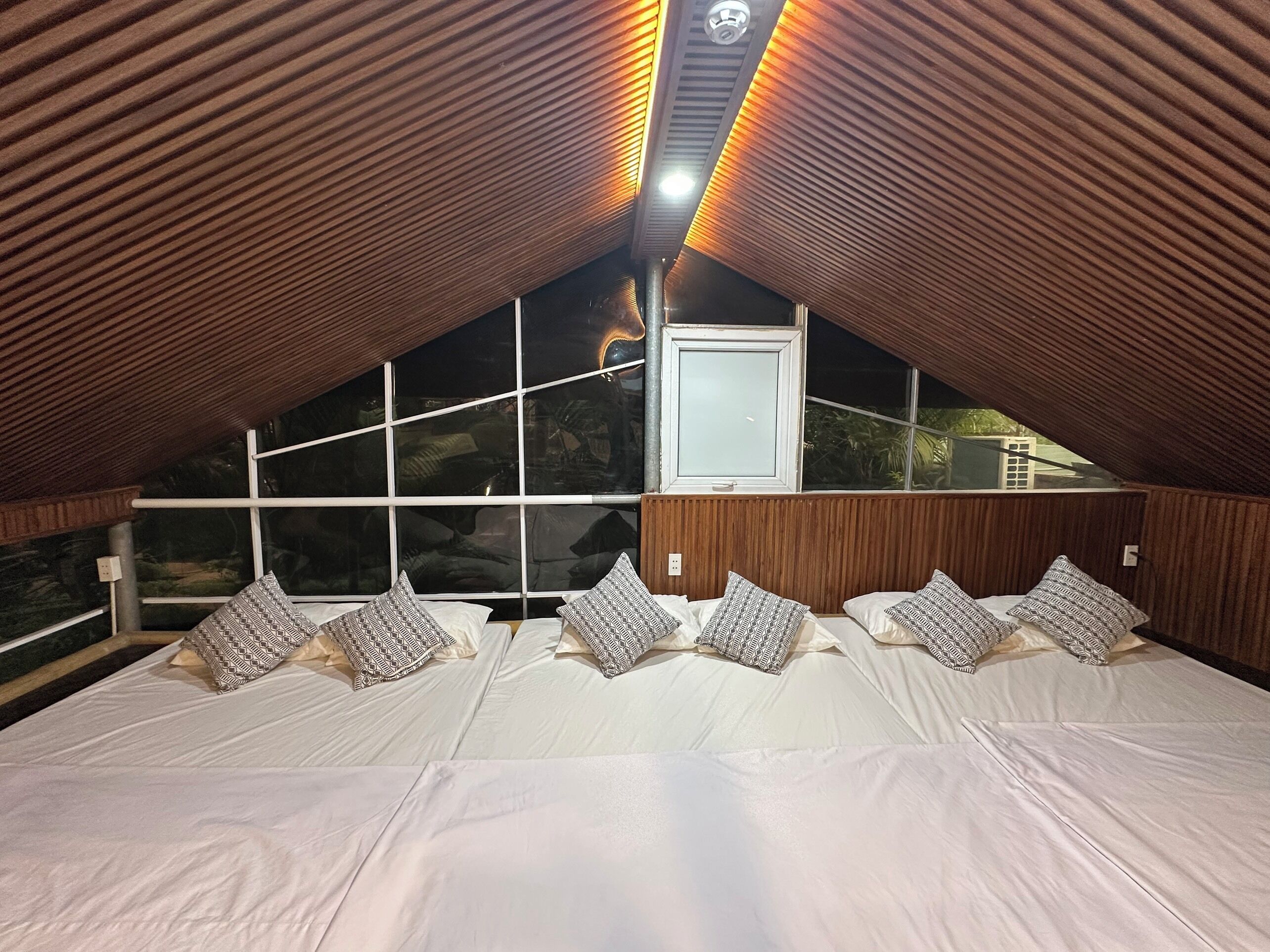 A bedroom with a sloped ceiling, a large window, and a bed with patterned pillows.