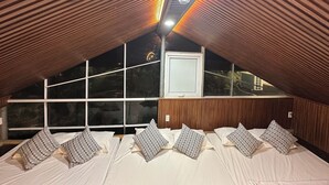 A bedroom with a sloped ceiling, wooden paneling, a large window, and patterned pillows. - Ngoc Linh Villas Hotel (Hải Hòa)