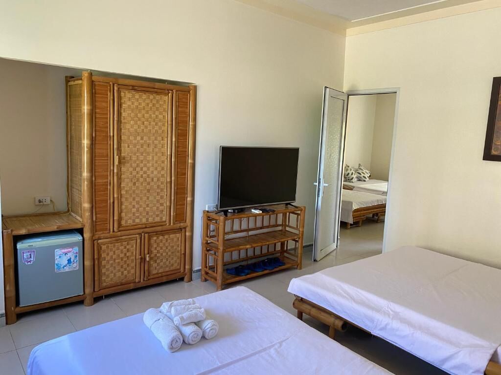 A hotel room with two beds, a television on a wooden stand, a wardrobe, and a small refrigerator.