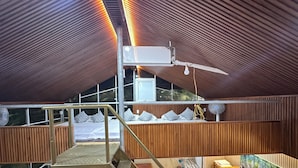 A modern interior with a wooden ceiling, a staircase, a bed with pillows, a table with items, and a fan. - Ngoc Linh Villas Hotel (Hải Hòa)