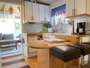 A compact kitchen with a central island, a dining area with a sofa, and a view of the outdoors. - 4 Star Holiday Home in Hollviken (Hollviken)
