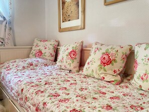 A bed with floral bedding and matching pillows, a framed picture on the wall, and a window with curtains.