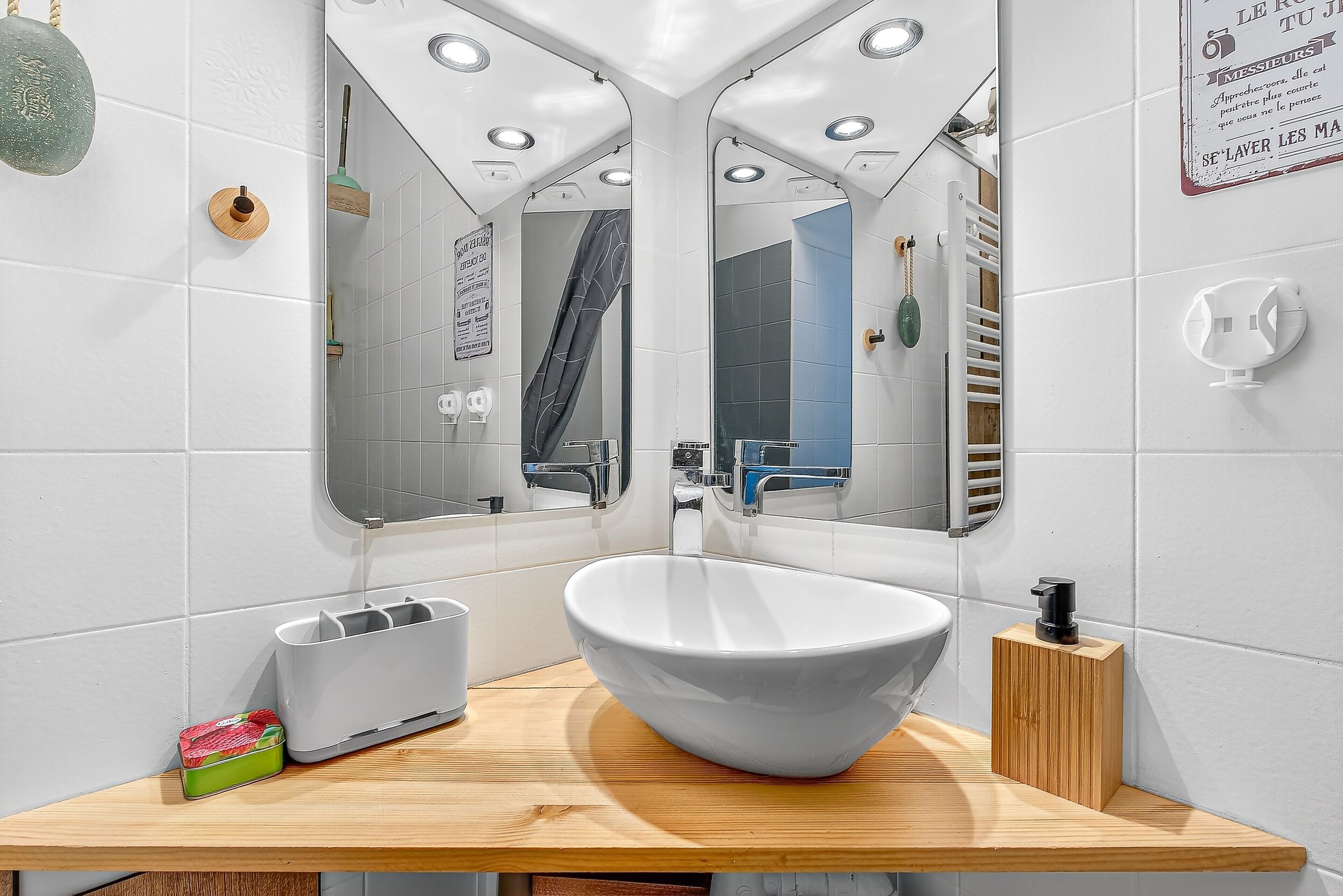 A modern bathroom with a large mirror, white tiles, a wooden vanity, and a white sink.