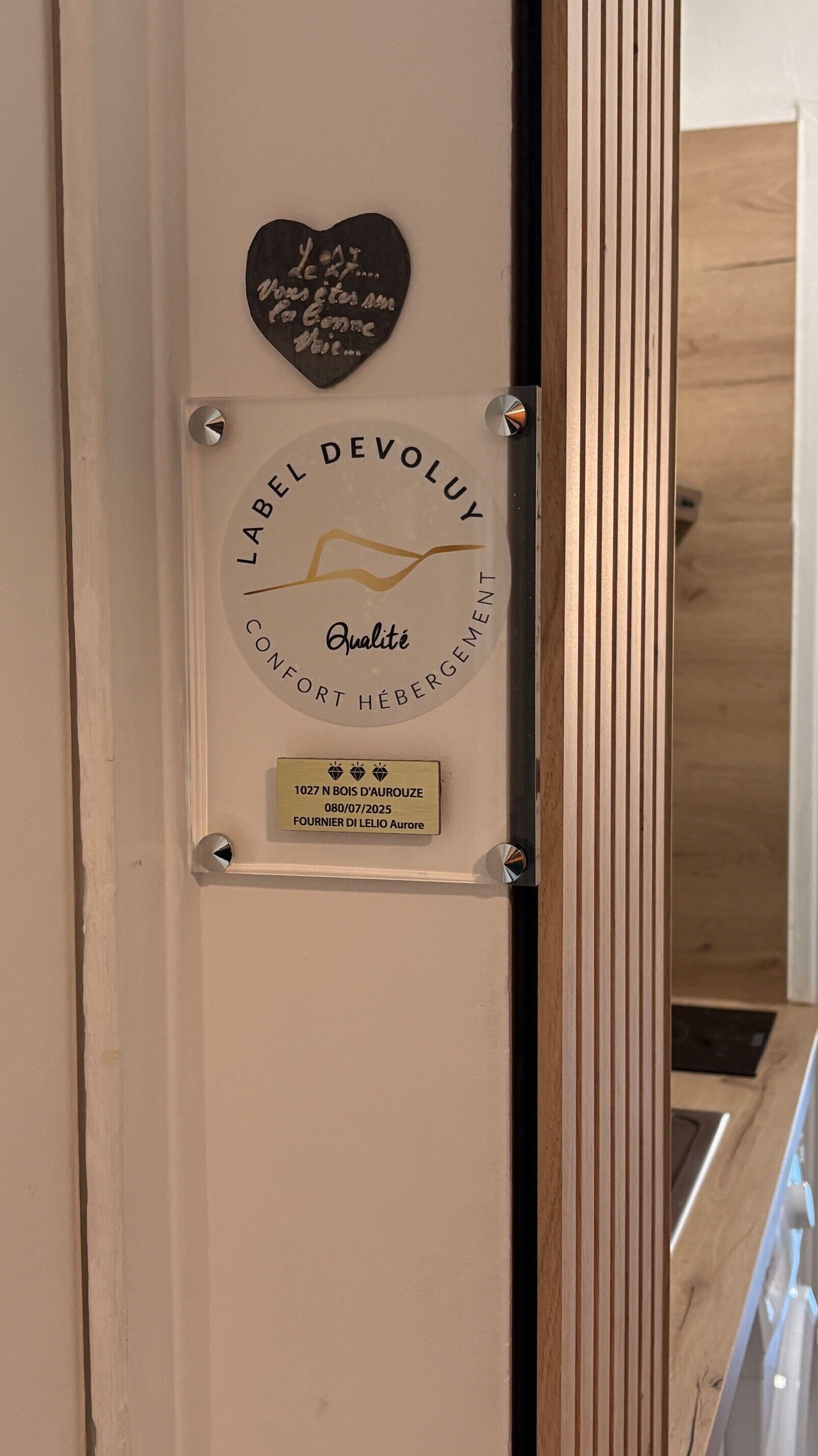 A plaque with 'Label Devoluy' and 'Qualité' text, a heart-shaped sign with text, and a small gold plaque with address and date.