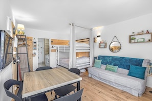 Une pièce de taille modeste comprenant un lit superposé, un canapé, une table à manger avec des chaises et un miroir au mur.