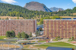 Un hotel de varios pisos, zona de estacionamiento y montañas al fondo.