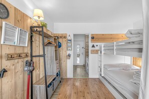 Habitación con literas, pared de madera, lámpara, reloj y zona de lavandería.