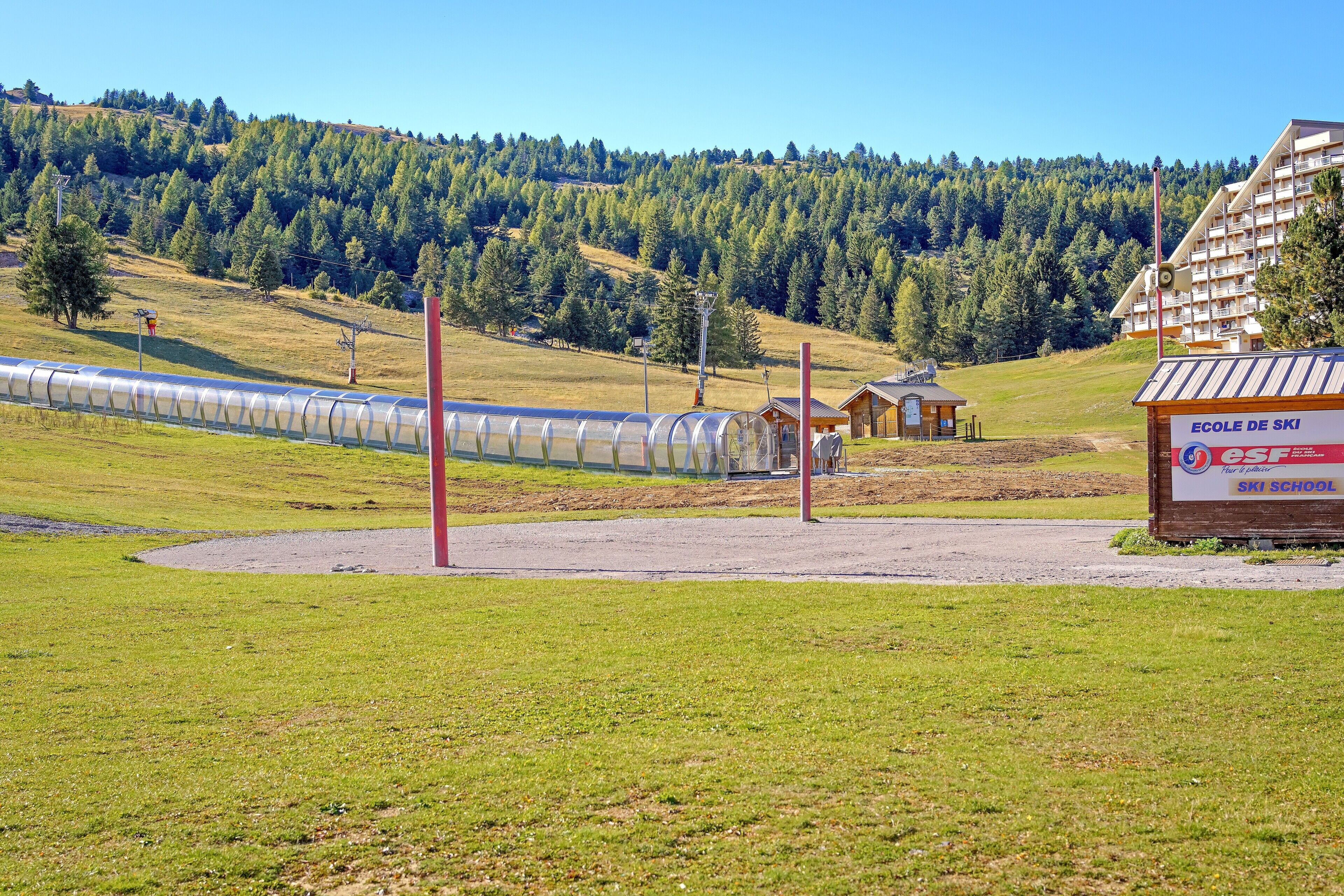 A ski school building with a sign, a ski lift, and a forested hill in the background.