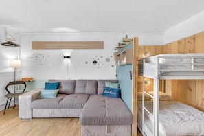 Una habitación moderna con sofá modular, literas, estante montado en la pared y decoración mural.