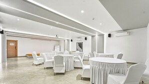 Une salle de conférence moderne, dotée de tables rondes et de chaises blanches, et équipée de luminaires au plafond et d’un système de climatisation.