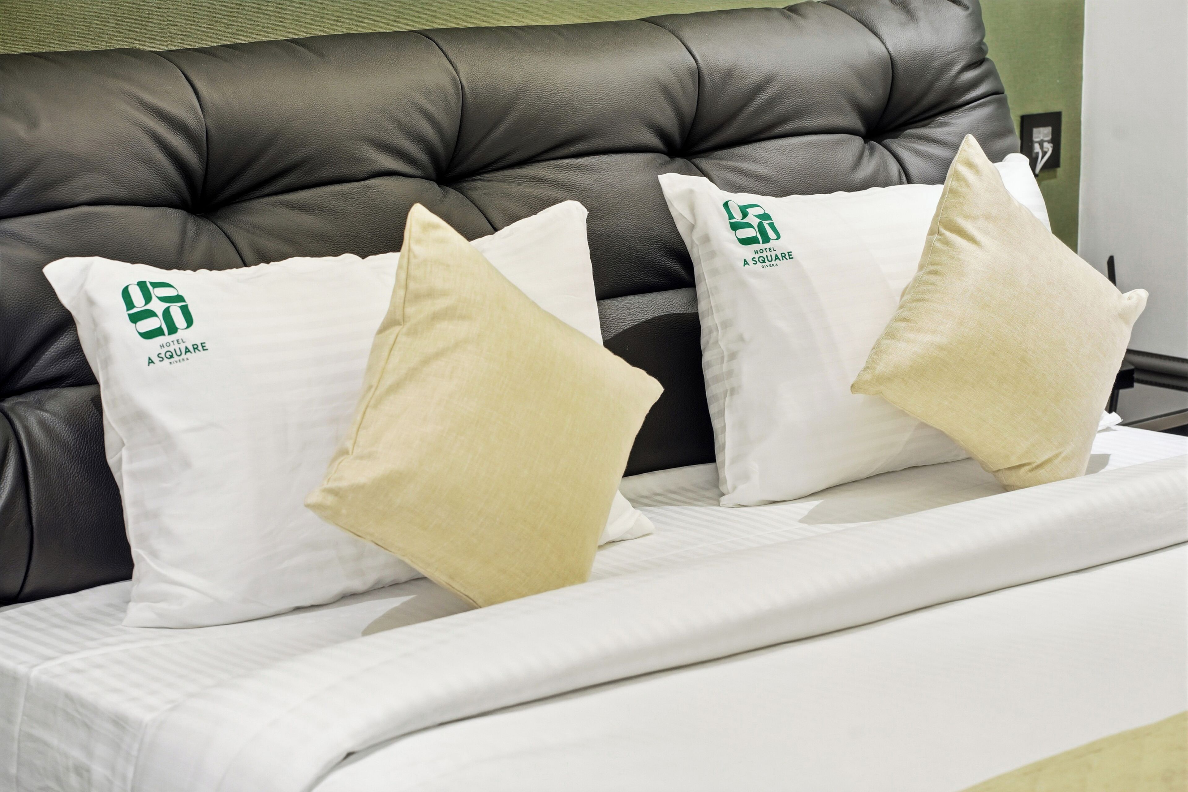 A bed with a black headboard and white bedding. There are two pillows with a logo and text on them.