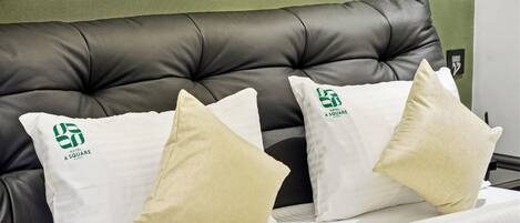 A bed with a black headboard and white bedding. There are two pillows with a logo and text on them.